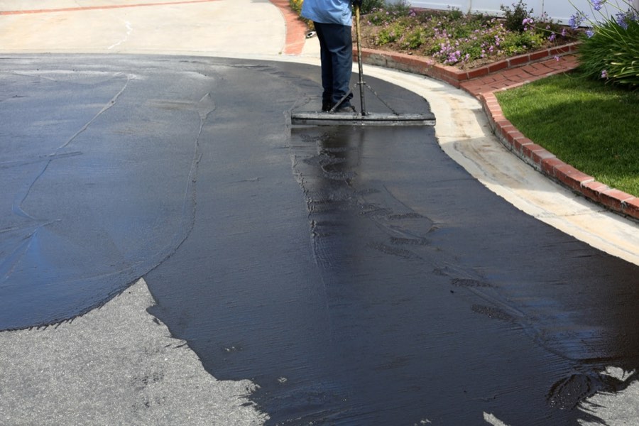 Worker squeegeeing fresh black sealcoat across a driveway